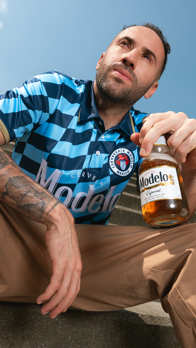David Ospina holding a Modelo beer bottle against a blue sky background