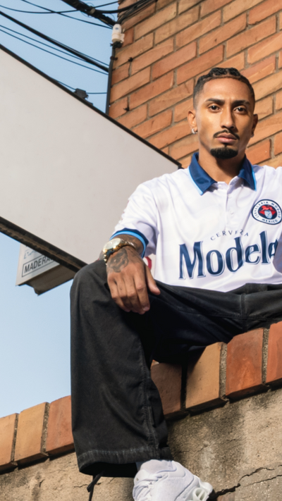 Raphina wearing a white shirt with 'Modelo' branding, sitting on a brick wall.