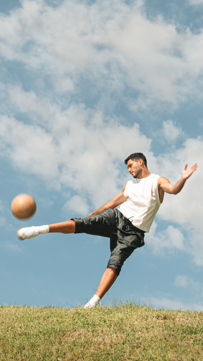Raúl Jiménez kicking a soccer ball in an open field with a blue sky